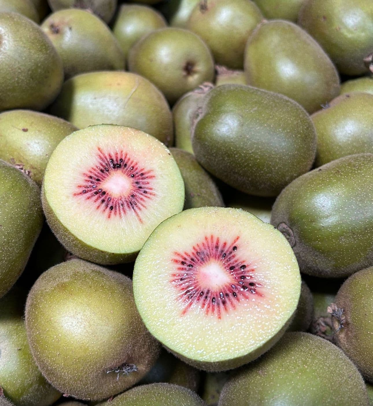 Kiwi rossi interi e tagliati a metà con polpa gialla e centro rosso brillante.