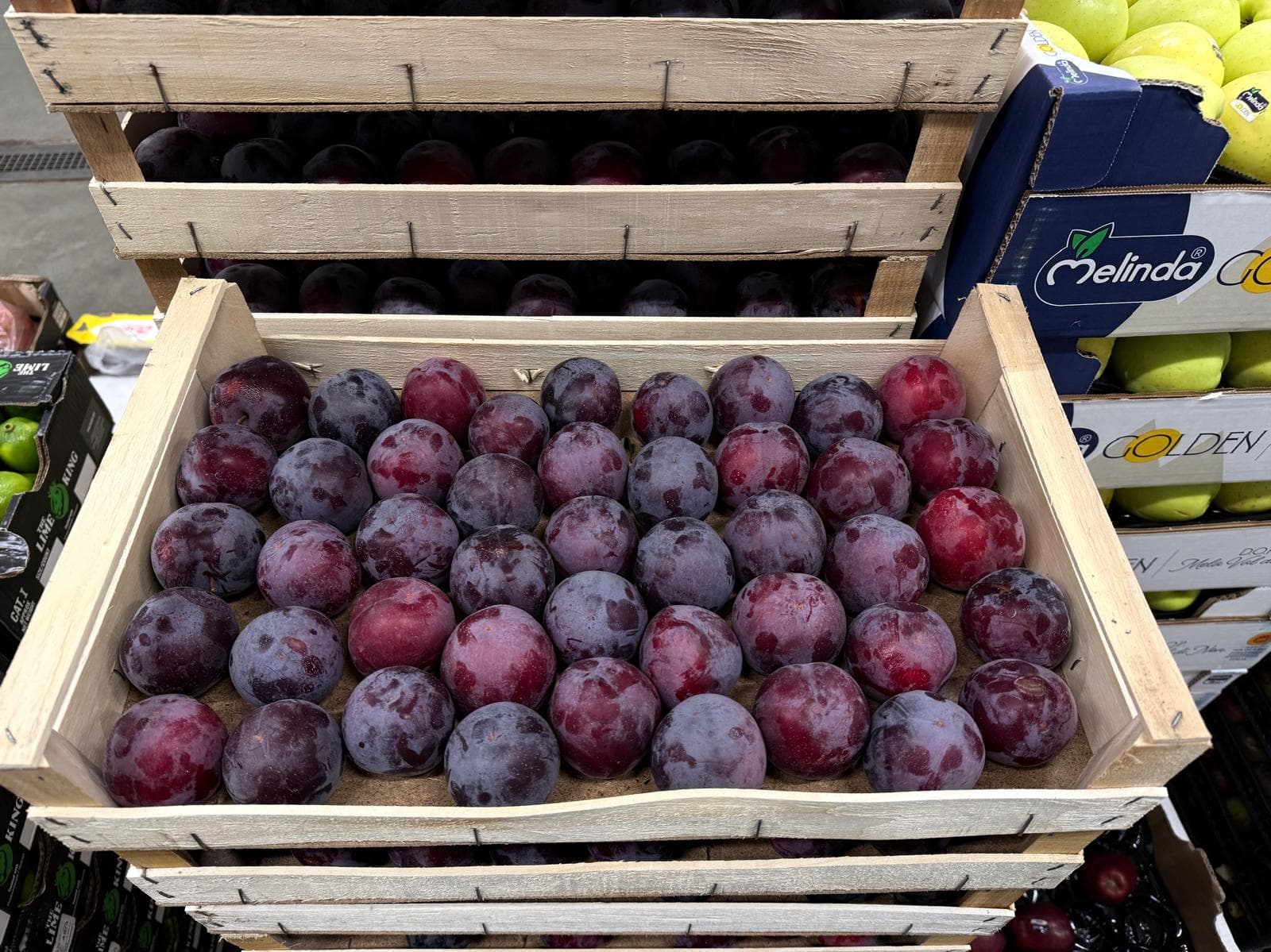 Cassetta di legno colma di prugne mature di colore viola scuro e rosso intenso.